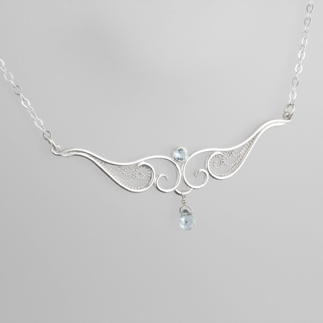 A graceful silver necklace with delicate filigree wirework, accented with sky blue topaz, on a light background.