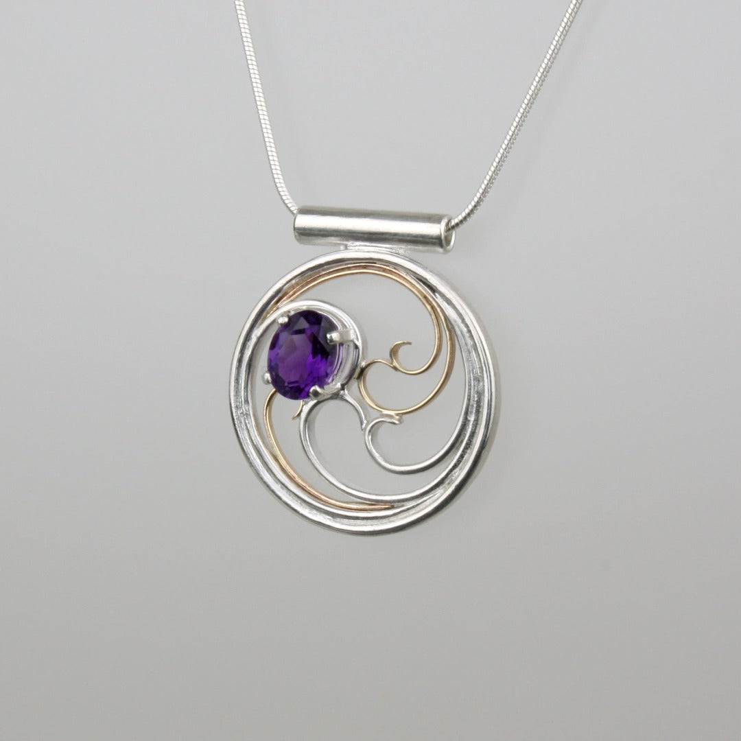 A circular pendant with cascading silver and gold waves encircling a deep purple oval amethyst gem.