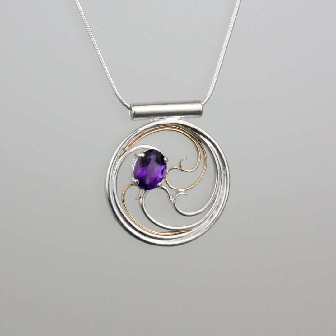 A circular pendant with cascading silver and gold waves encircling a deep purple oval amethyst gem.