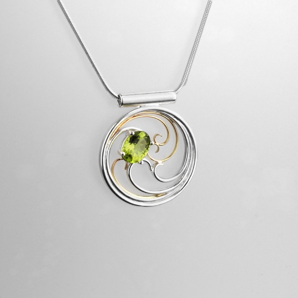 A circular pendant with cascading silver and gold waves encircling a brilliant green oval peridot gem.