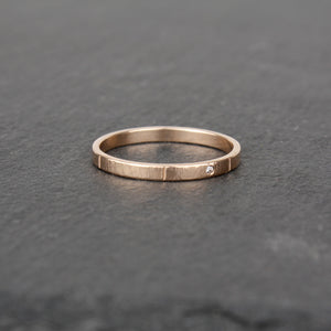A slender ring made of 14k rose gold on a slate stone. The ring has a tiny sparkling diamond (1mm size) embedded in the metal. The ring has a hammered surface that catches the light.