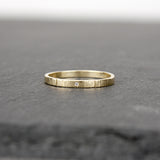 A slender ring made of 14k yellow gold on a slate stone.  The ring has a tiny sparkling diamond (1mm size) embedded in the metal.  The rings have a hammered surface that catches the light.