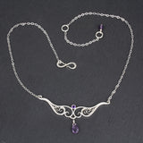 A graceful silver necklace with delicate filigree wirework, accented with purple amethyst, on a slate stone background.