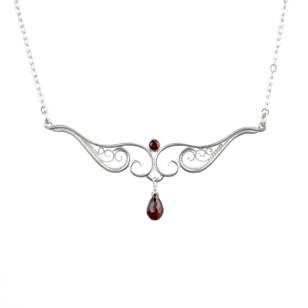A graceful silver necklace with delicate filigree wirework, accented with deep red garnet, on a light background.
