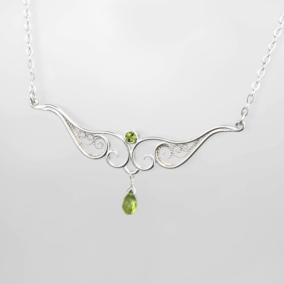 A graceful silver necklace with delicate filigree wirework, accented with green peridot, on a light background.