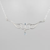 A graceful silver necklace with delicate filigree wirework, accented with sky blue topaz, on a light background.