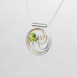 A circular pendant with cascading silver and gold waves encircling a brilliant green oval peridot gem.