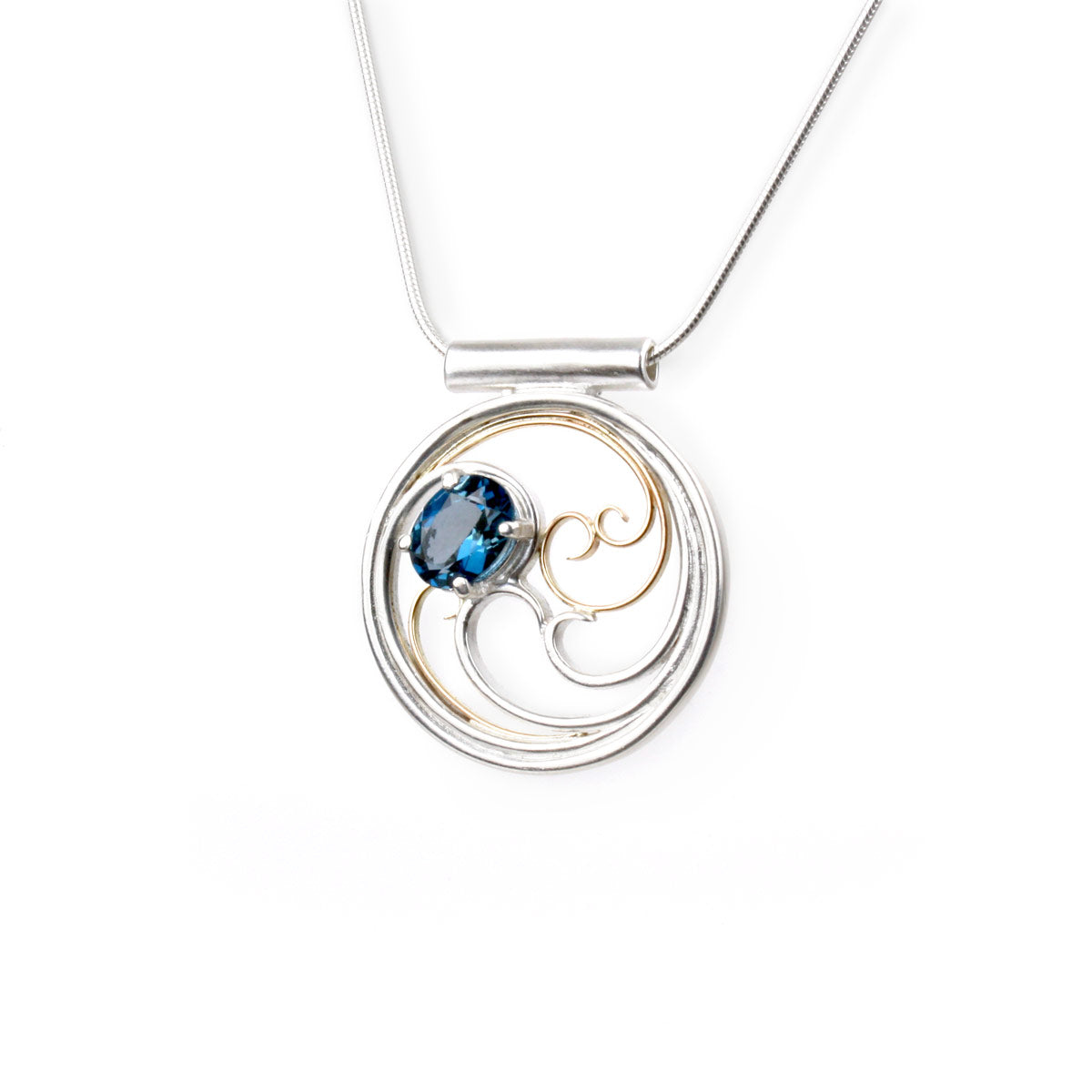 A circular pendant with cascading silver and gold waves encircling a deep blue oval topaz gem.