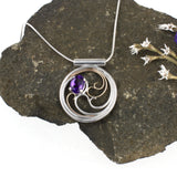 A circular pendant with cascading silver and gold waves encircling a deep purple oval amethyst gem.